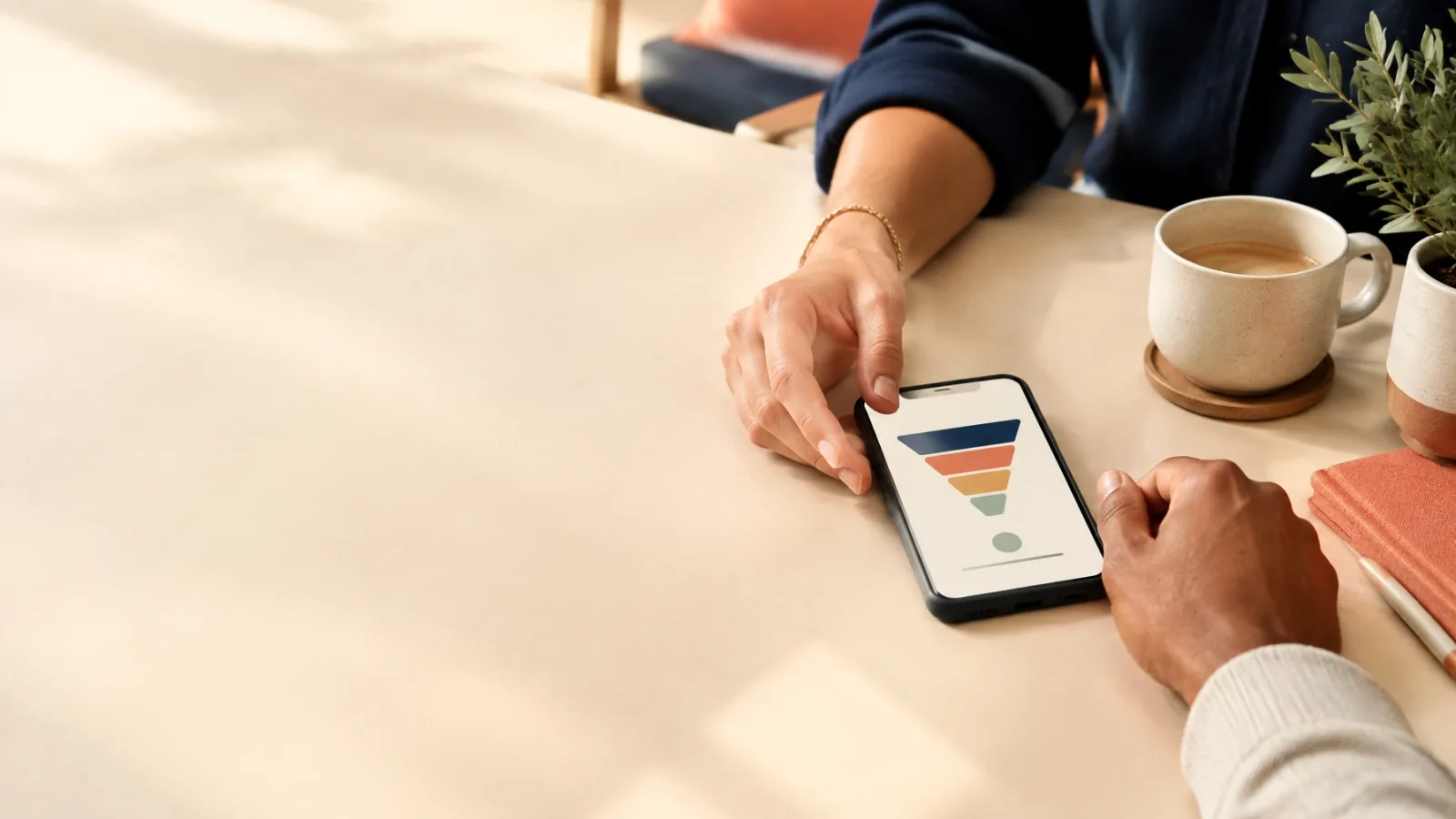 Two people reviewing a simple conversion funnel on a phone across a warm cream table